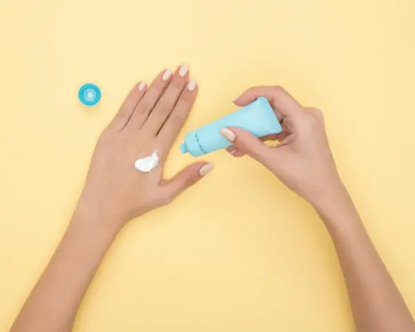 Hände mit Creme, die Glycerin enthält, auf gelbem Hintergrund.