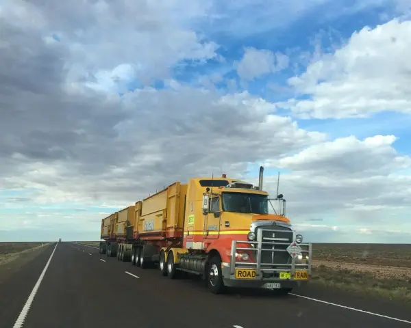 Żółta ciężarówka typu road train z naczepami na pustej drodze pod zachmurzonym niebem.