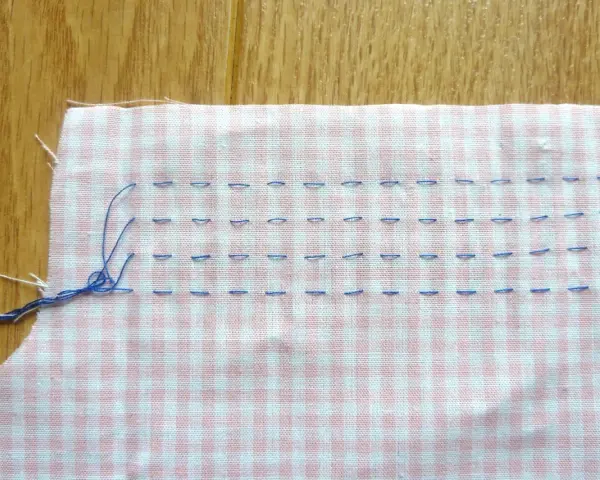 Tissu à carreaux rose et blanc avec des points de couture bleus, préparant un smock couture.