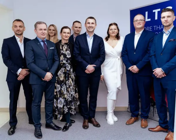 Grupa osób w garniturach i sukience pozuje do zdjęcia na tle banera.