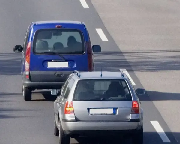 Un veicolo che precede, una monovolume blu, è seguito da un'auto station wagon argentata su una strada asfaltata con segnaletica bianca.