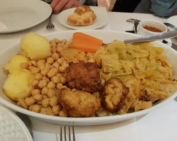 Un plato generoso de cocido madrileño con garbanzos, patatas, zanahoria, repollo y trozos de carne frita.