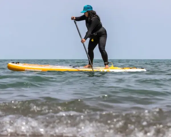 Frau auf einem gelben Stand Up Paddle Board im Meer, mit Paddel in der Hand.