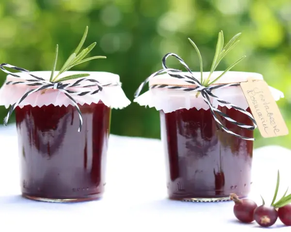 Zwei Gläser Jostabeere-Marmelade, liebevoll mit Rosmarin und kariertem Band verziert. Perfekt für die Jostabeere Verwendung auf Brot.