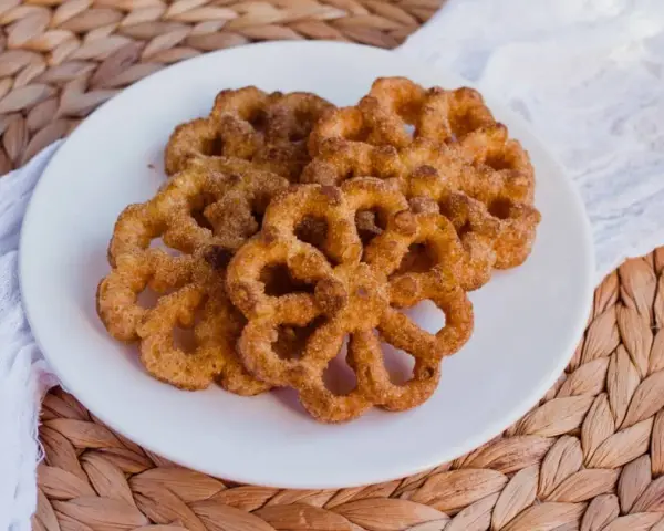 Buñuelos dorados con azúcar y canela en un plato blanco.