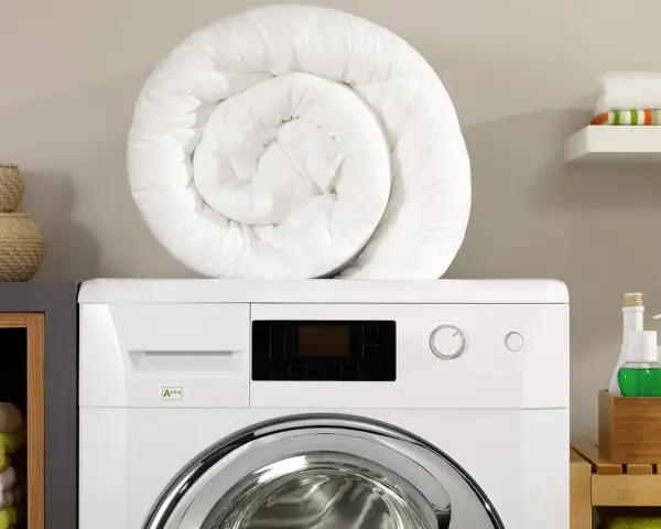 Piumone bianco arrotolato sopra una lavatrice. Pronto per essere lavato in lavatrice a 40 gradi per un bucato fresco e pulito.