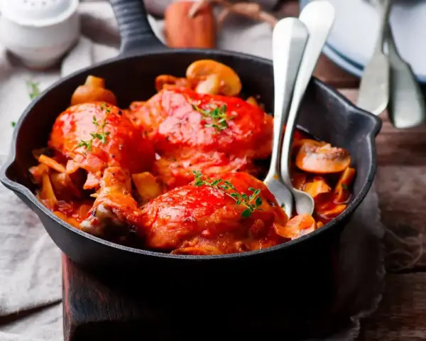 Pollo alla Marengo succulento in padella con funghi e pomodoro, guarnito con timo fresco.