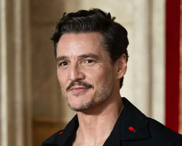 Pedro Pascal con cortes de pelo hombre corto por los lados y largo arriba, luciendo un pin de cerilla en su solapa.