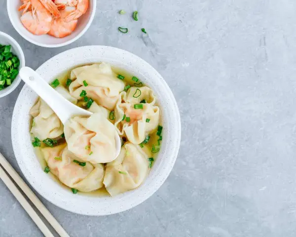 Aksamitna zupa wonton z krewetkami i szczypiorkiem, podana z pałeczkami.
