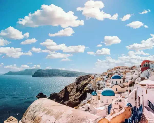 Santorini, Grecja. Białe domy z niebieskimi kopułami na klifie nad morzem. Zastanawiasz się, ile się leci do Grecji?