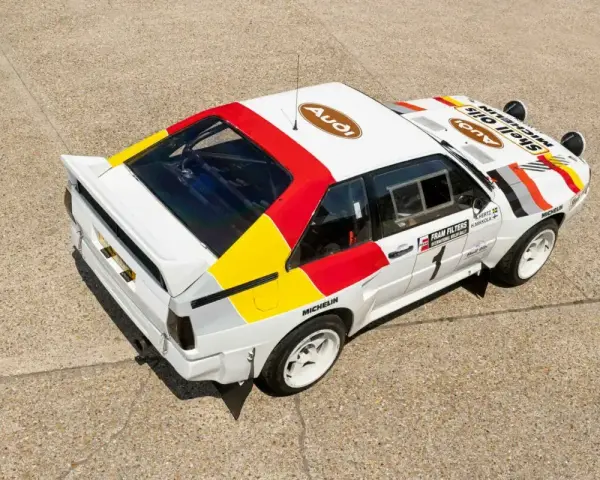 Biały rajdowy **Audi quattro S1** z kolorowymi pasami i logotypami sponsorów, gotowy do podboju szutrowych tras.