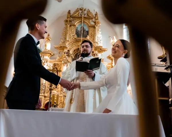 Para młoda ściska dłoń księdza podczas ceremonii. Zastanawiasz się, ile trwają nauki przedmałżeńskie?