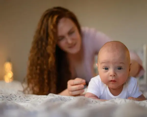 Maluch ćwiczy mięśnie szyi, kiedy układać noworodka na brzuchu. Mama czuwa z tyłu.