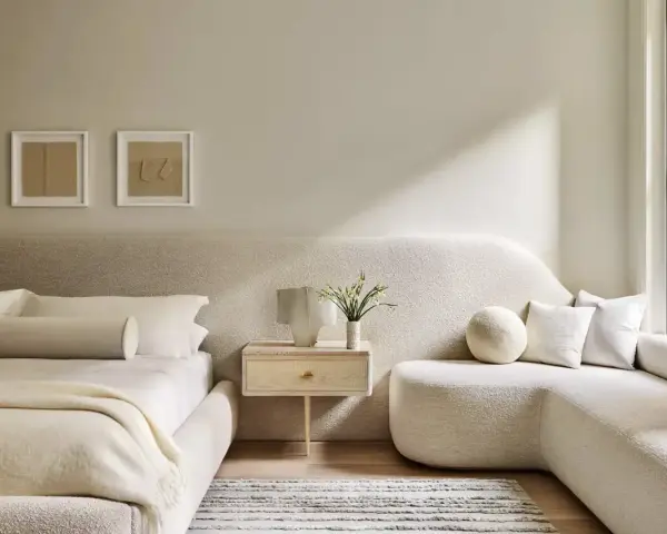 Dormitorio con decoración minimalista, cama baja, sofá curvo y arte abstracto en tonos tierra.