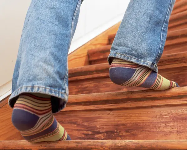 Füße in bunten Socken steigen eine Holztreppe hinauf, die auf eine Renovierung wartet.