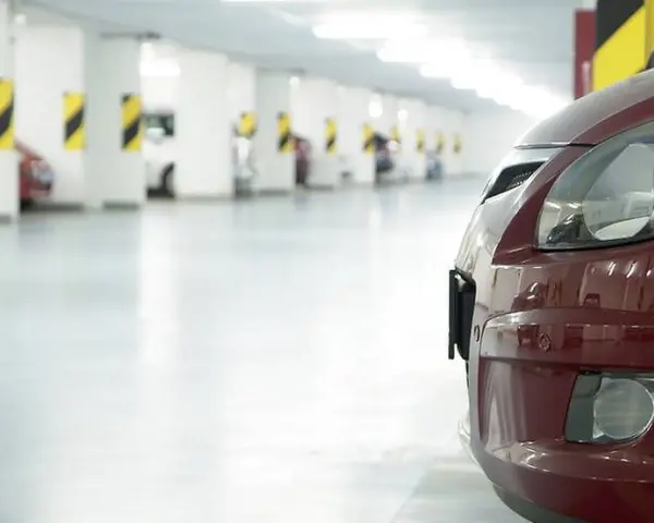 Czerwony samochód na tle rzędu miejsc parkingowych. Zastanawiasz się, ile miejsc parkingowych na mieszkanie jest dostępne?