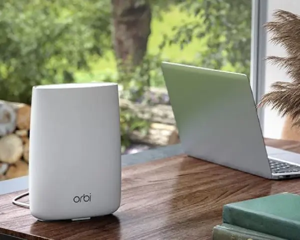 Ein weißer Orbi WLAN-Router steht neben einem Laptop auf einem Holztisch.