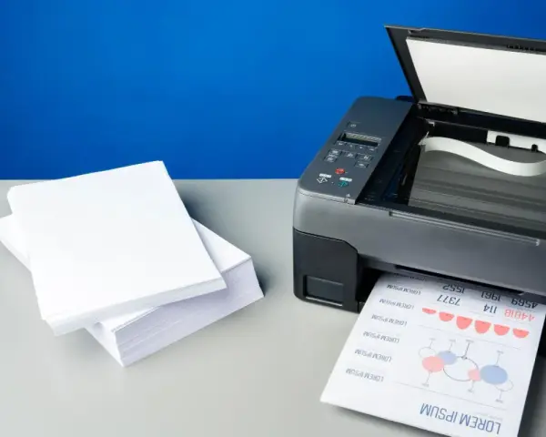 Stos białego papieru obok drukarki, która właśnie drukuje dokument. Różne rodzaje papieru do druku.