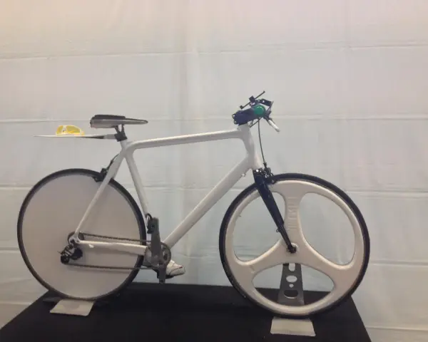 A sleek, white 3d printed bike with unique disc and tri-spoke wheels. Yellow sunglasses rest on the seat.