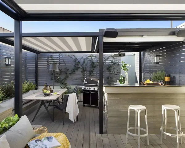 Porche moderno con mesa, parrilla y una barra de bar, ideal para disfrutar de una cocina exterior.