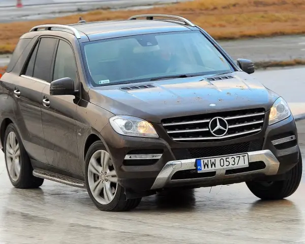 Brązowy Mercedes-Benz ML na mokrej nawierzchni, z widoczną tablicą rejestracyjną WW 0537T.