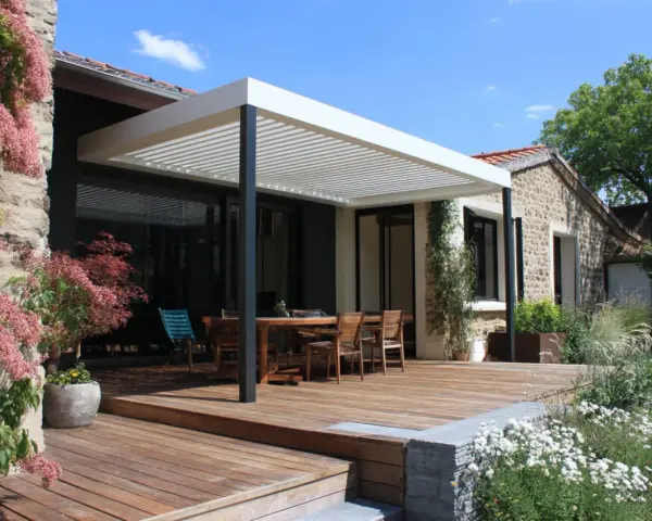 Une belle terrasse tropezienne en bois avec mobilier de jardin sous une pergola moderne. Le soleil brille sur la végétation luxuriante.