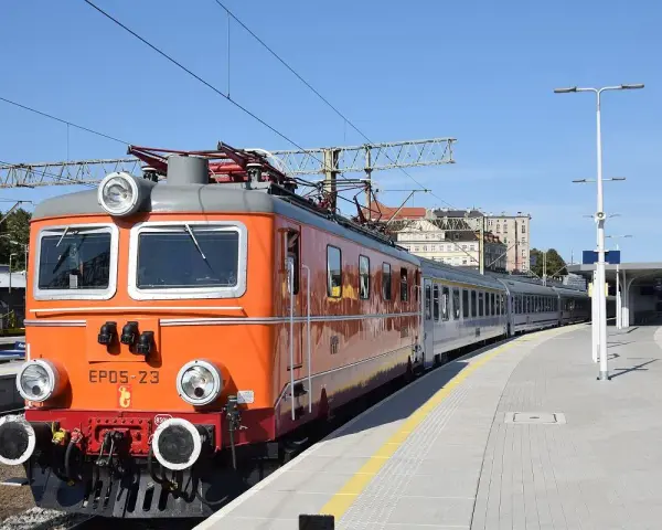 Pomarańczowa lokomotywa EP05-23, znana jako "eic chrobry", stoi na stacji. Pociąg jest gotowy do podróży.