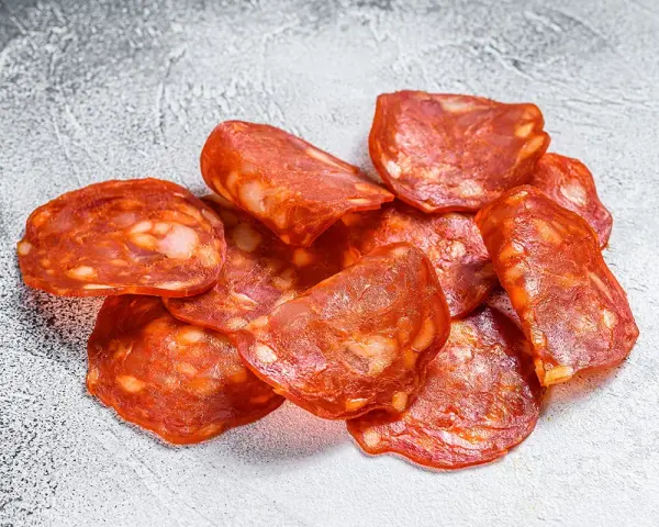 Plasterki pikantnego chorizo, wędzonej kiełbasy wieprzowej, z widocznymi kawałkami tłuszczu.
