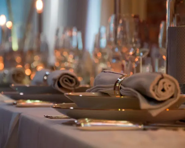 Ett elegant dukat bord med rullade servetter, hållna av en gyllene organza band-liknande ring. Mjuk belysning skapar en varm atmosfär.