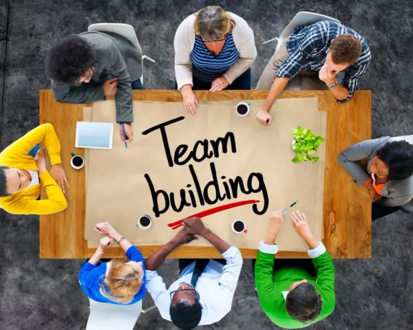 Un groupe diversifié autour d'une table discute de "team building". Ils collaborent, partageant des idées pour renforcer leur unité.