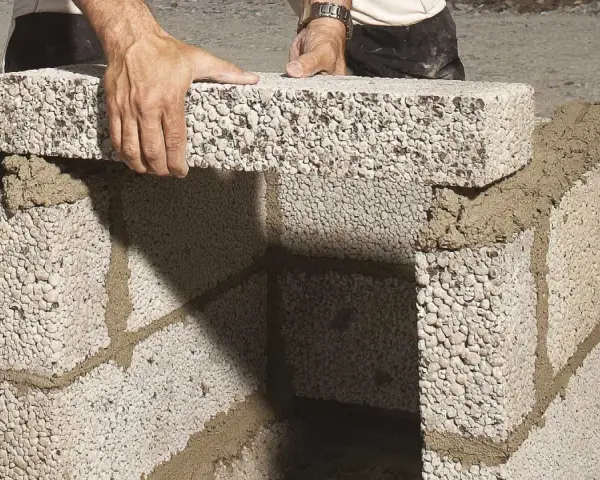 Byggare lägger mura lecablock på betongplatta. Murbruket syns mellan blocken.