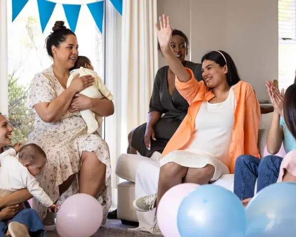 Glada kvinnor firar en babyshower med ballonger och bebisar. En kvinna vinkar glatt.