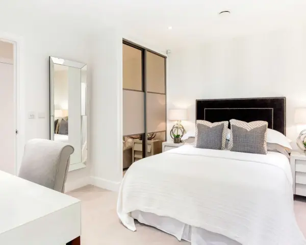 Elegante camera da letto senza finestra, con letto bianco, specchio a figura intera e un angolo toeletta.