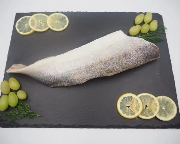Filet ryby na czarnej desce z plasterkami cytryny, winogronami i koperkiem.