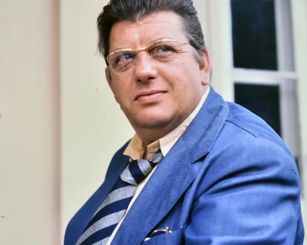Portret Mariusza Dmochowskiego w okularach i niebieskiej marynarce. W tle okno.