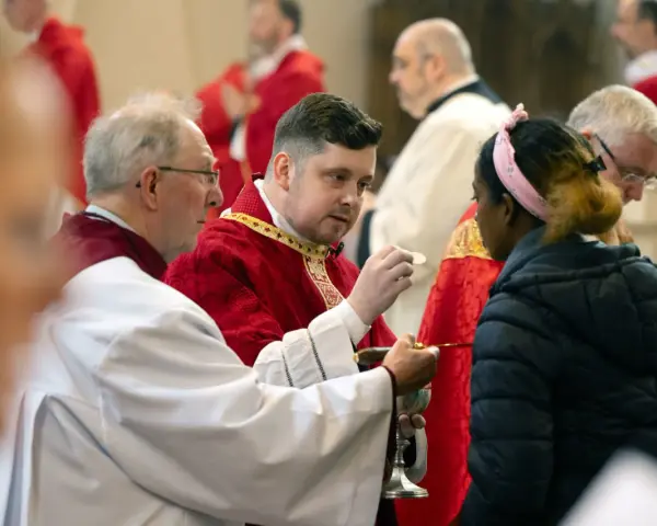 Clergy in red robes perform communion, a sacred act that can be seen as a form of evangelizing, sharing faith with a young woman.