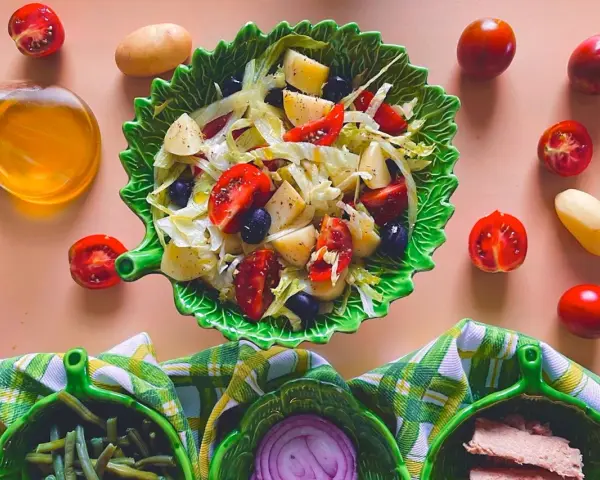 Un'insalata di patate napoletana colorata con pomodorini, olive e lattuga, servita in una ciotola a forma di foglia.