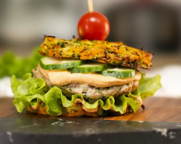 Burger z warzywną bułką, kotletem, ogórkiem, sosem i pomidorkiem na wykałaczce.