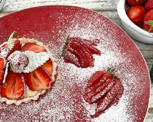 Zuckersüße Erdbeer Tartelettes, bestäubt mit Puderzucker, auf rotem Teller. Daneben frische Erdbeeren und eine Gabel.
