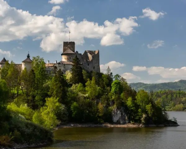 Zamek w Czorsztynie góruje nad jeziorem, otoczony zielenią. W oddali widać góry.