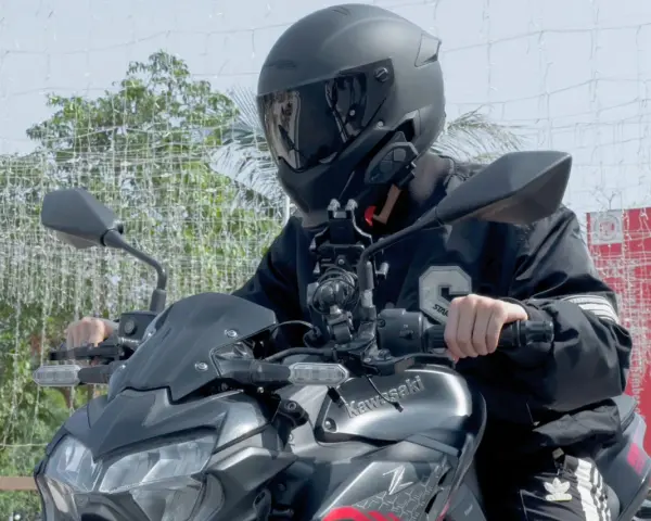 Motocyklista w kasku siedzi na motocyklu Kawasaki, z zamontowanym interkomem na kasku.
