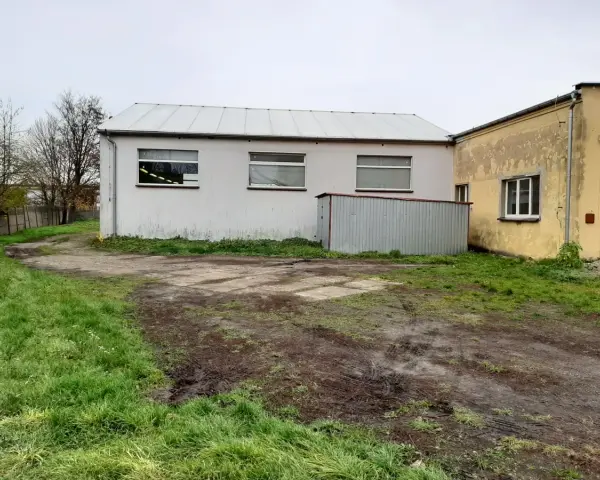 Teren wokół budynków jest nierówny, z błotnistymi śladami i trawą. Widać tu różne formy terenu, od płaskich placów po lekko nachylone trawniki.