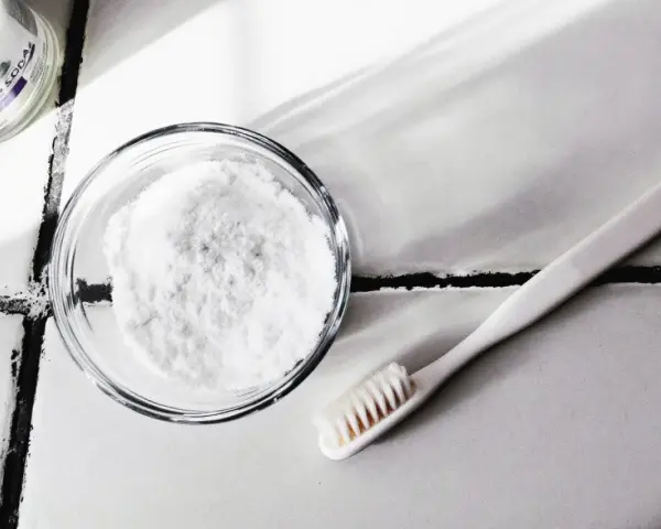 Bicarbonate de soude dans un bol et une brosse à dents sur un carrelage.