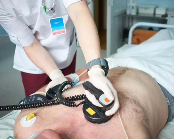 Ratownik medyczny wykonuje kardiowersję u pacjenta leżącego w łóżku szpitalnym, używając defibrylatora.