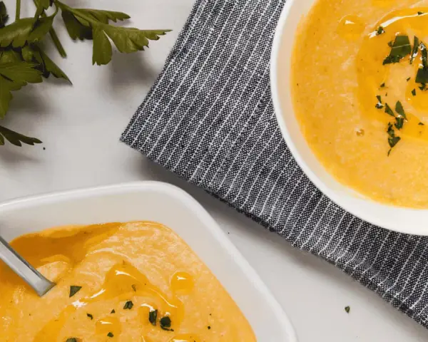 Deux bols de velouté de butternut facile, ornés d'huile d'olive et de persil frais, prêts à être dégustés.