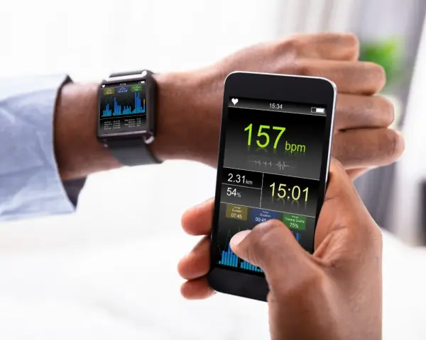 Mężczyzna sprawdza na smartfonie i zegarku dane treningowe: tętno 157 bpm, dystans 2.31 km. Zegarek mierzący ciśnienie pokazuje wykresy.