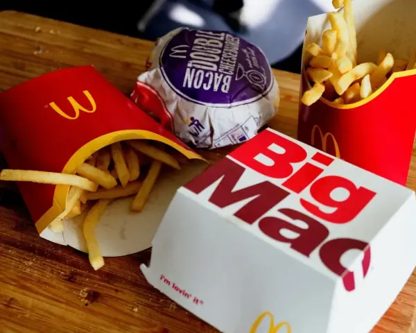 Frytki McDonald's w czerwonych opakowaniach i pudełko Big Mac na drewnianym tle.