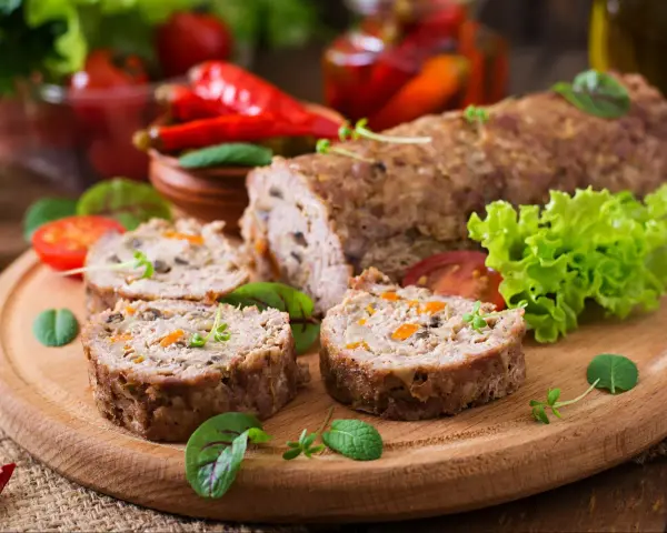 Pokrojone zrazy z mięsa mielonego z warzywami na desce, obok sałata, pomidory i papryczki chili.