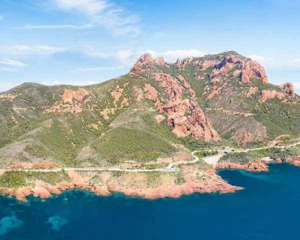 Strada panoramica sulla Corniche de l'Esterel, con montagne rosse e mare blu intenso.