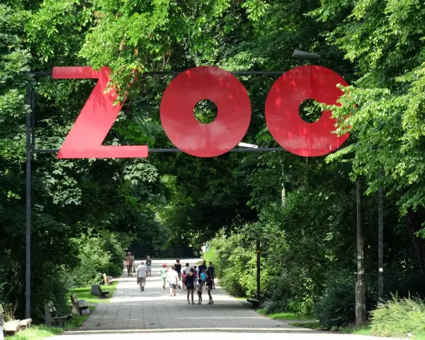 Duże czerwone litery "ZOO" nad alejką w parku. Wiele zoo w Polsce zaprasza na spacer.